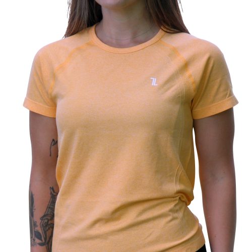 A woman with long brown hair wears the GlideFlex Tee - Tangerine and black leggings, standing confidently as she looks ahead. Her left arm has visible tattoos and she wears a smartwatch on her left wrist.