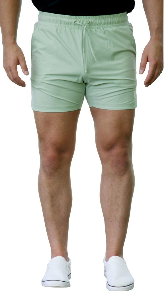 A person wearing HYDRX Swim Shorts - Waveleaf in light green, a black top, and white slip-on shoes stands with arms relaxed by their sides against a white background.