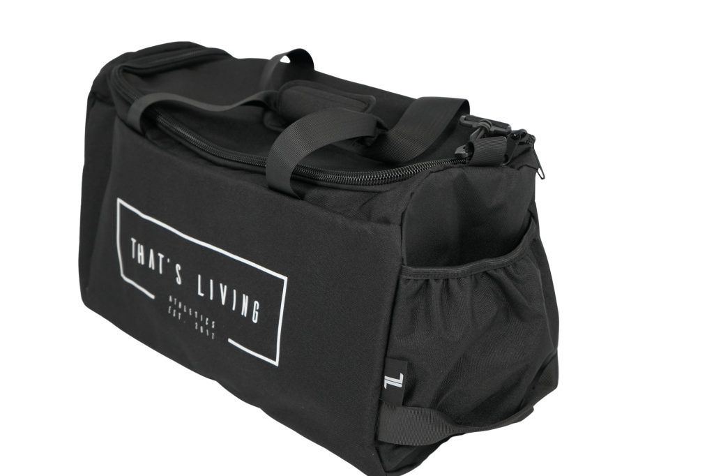 The TRIARC Duffle Bag is black with "THAT'S LIVING" in white on the front pocket. It features a side mesh pocket, carrying handles, and a zippered top, shown against a white background.